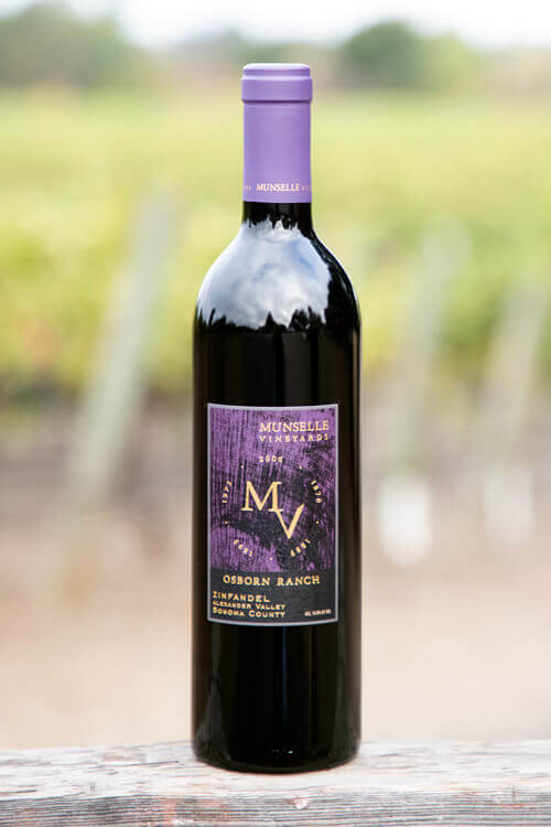 Munselle Vineyards Osborn Ranch Zinfandel with purple-colored label on a dark glass bottle, and a blurred vineyard background.